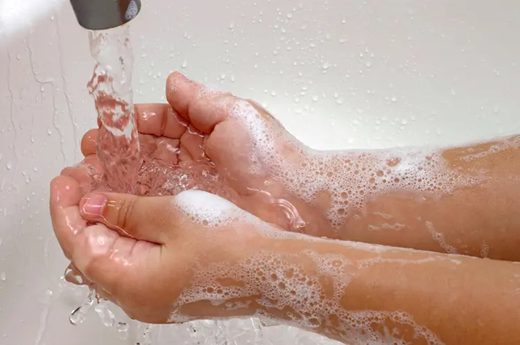 Childs hands covered with soap foam under running faucet