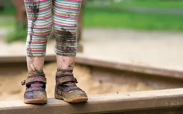 Legs and feet of muddy child in sand pit