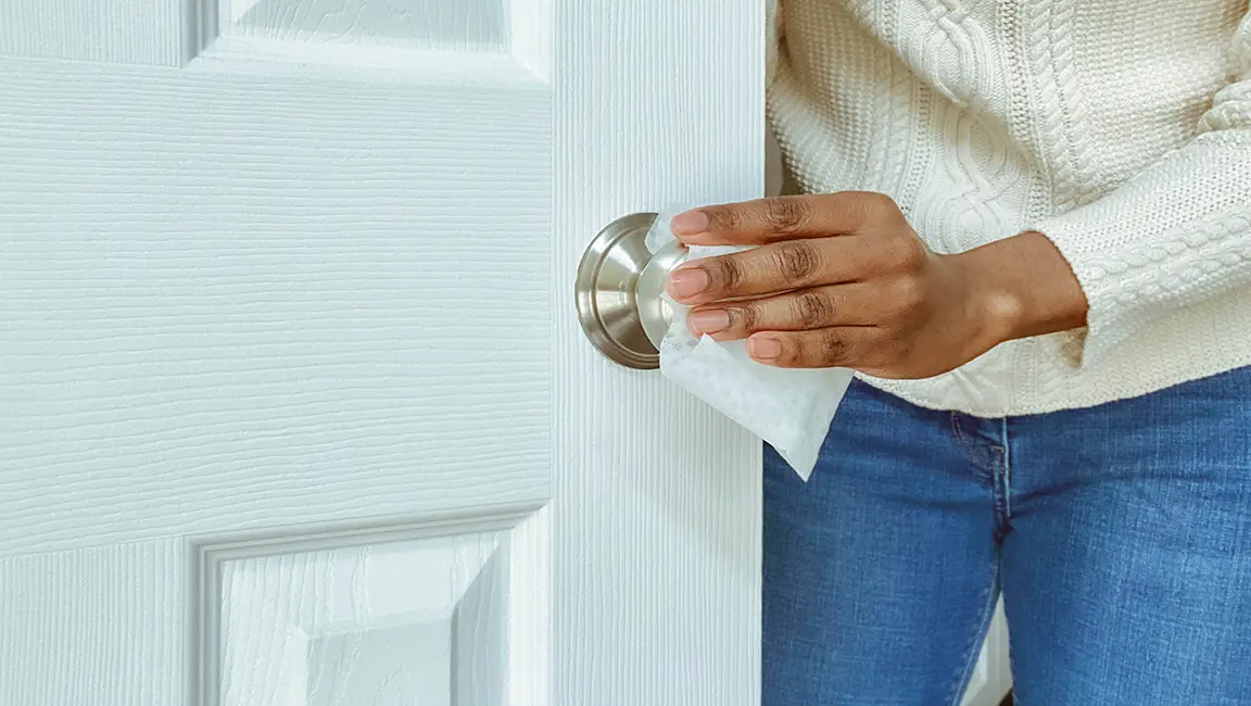 Person wiping the chrome doorknob of a white door