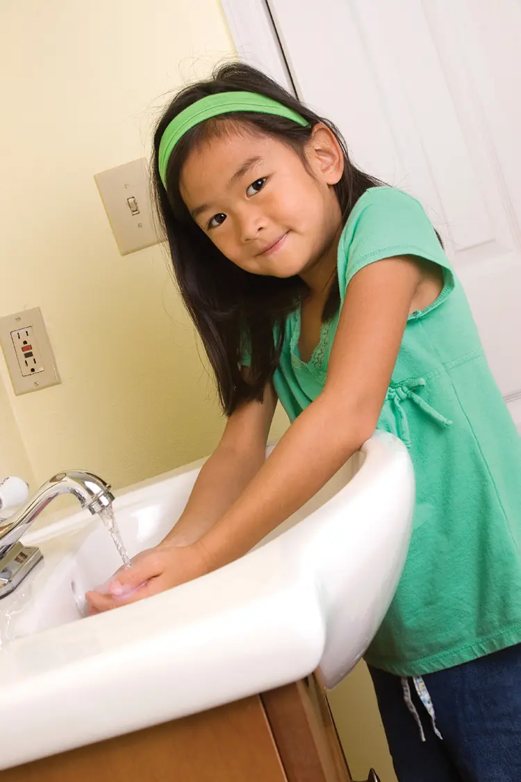 Child leans over bathroom sink with running faucet