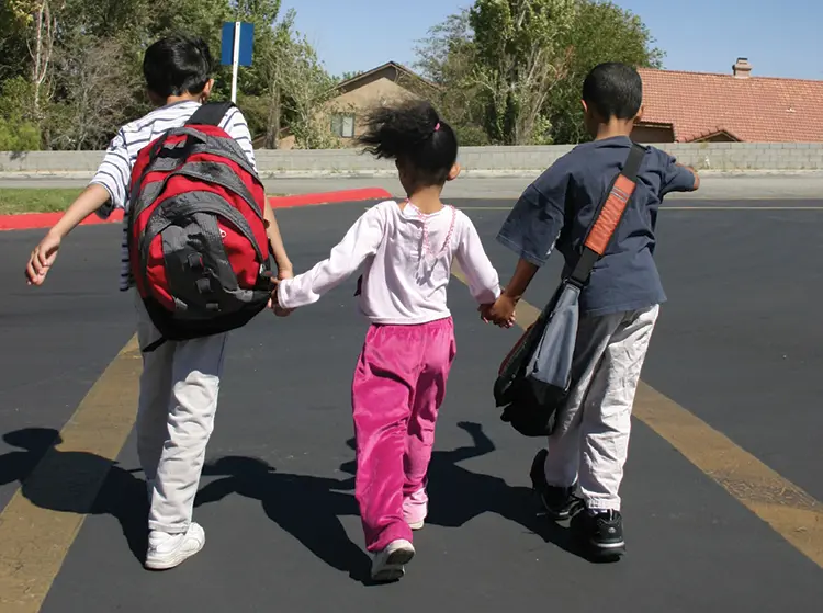 Three children on a school playground walking away and holding hands