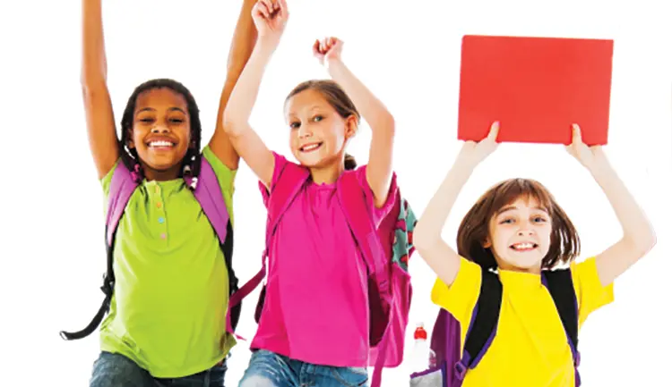 Children with backpacks holding hands and workbooks in the air and jumping
