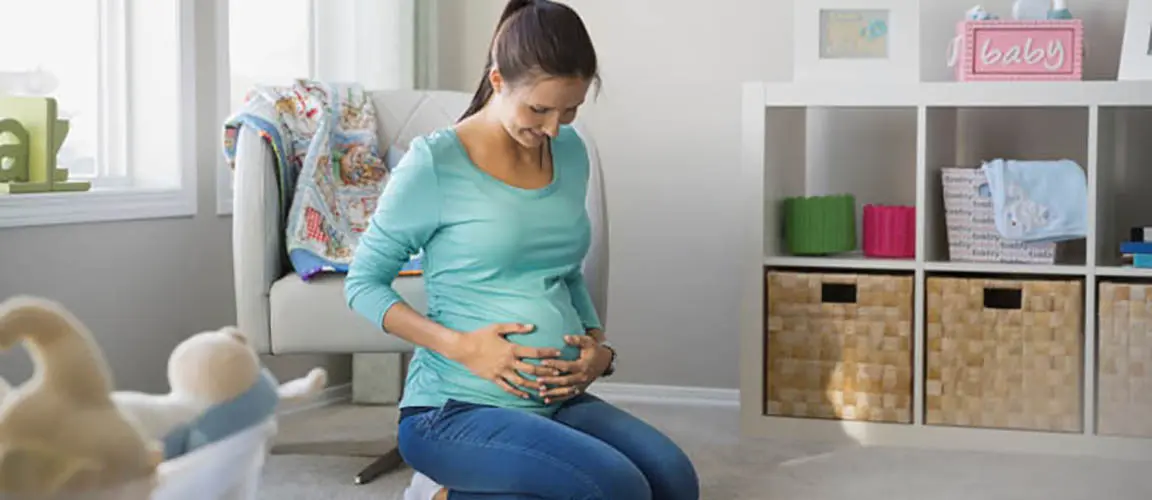 Pregnant woman kneeling on floor and holding baby bump