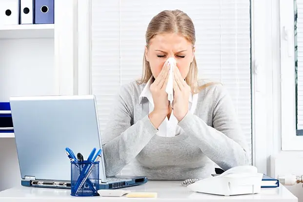 Person in office in front of laptop blows nose into tissue