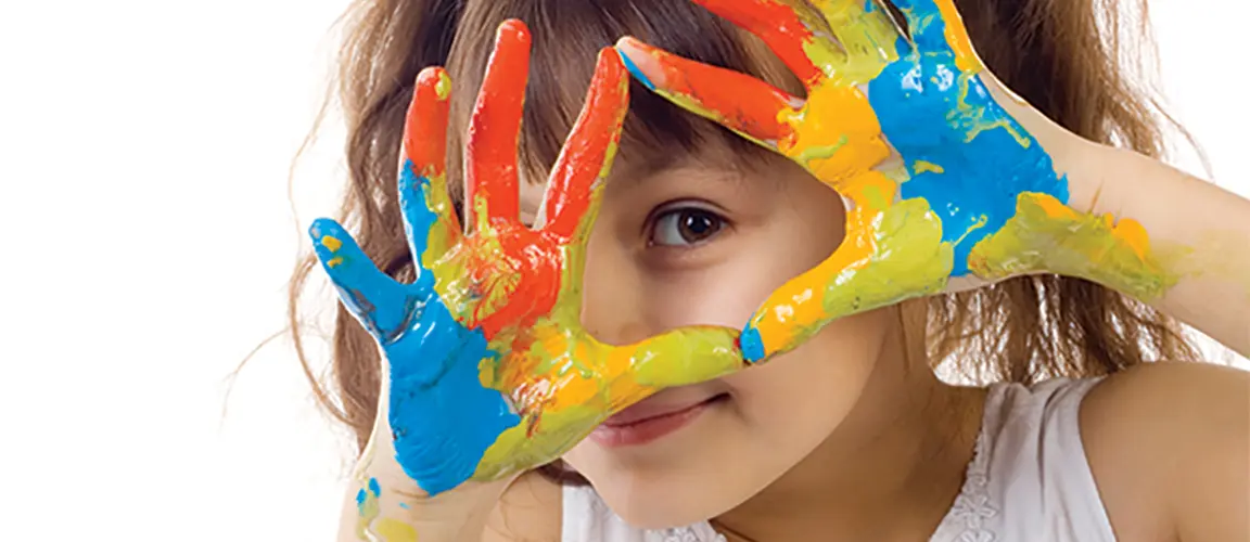 Child holding paint covered hands up to their face