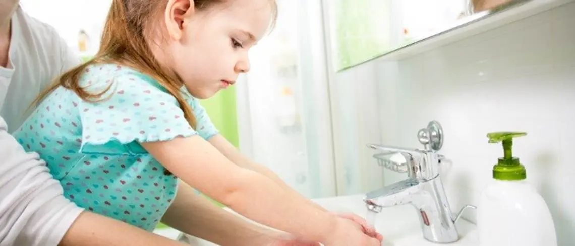 Parent helping child wash hands in bathroom
