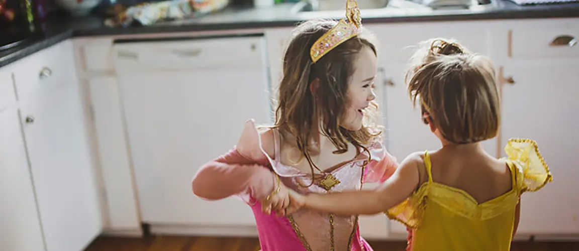 Two children in princess costumes dancing in a kitchen