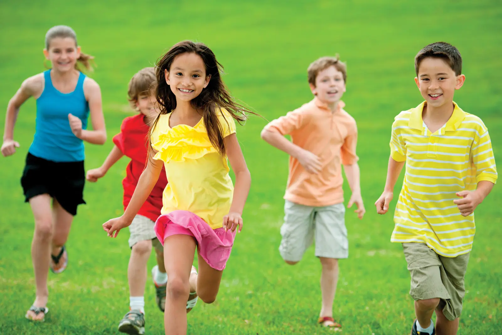Children in bright clothing running on green grass field