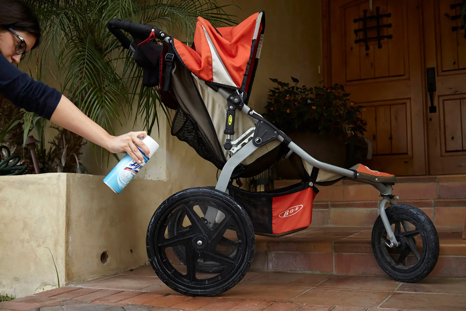 Person spraying the wheels of a stroller with Lysol Disinfectant Spray
