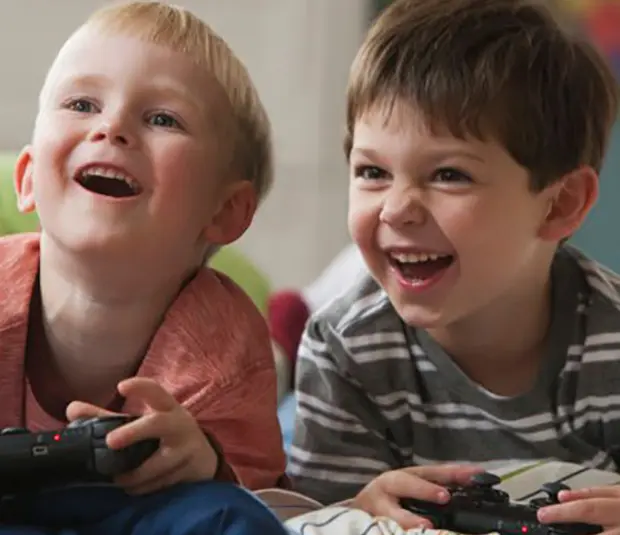 Children lying on bed holding gaming console controller and laughing