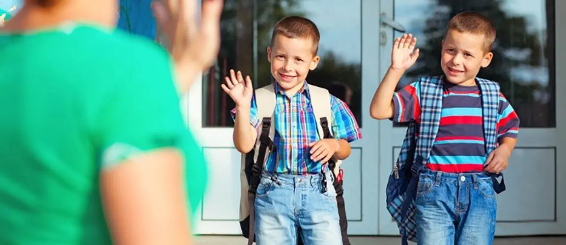 Parent waves goodbye to children with backpacks who are waving back