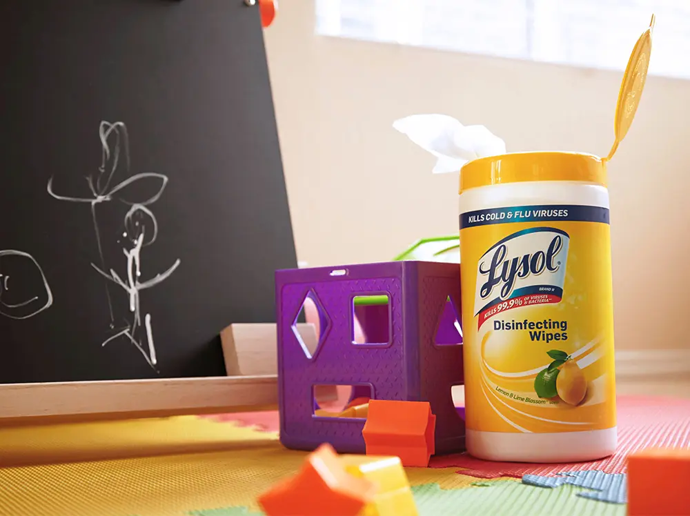 A canister of Lysol Disinfecting Wipes on the floor of a playroom next to a chalkboard and some baby toys.
