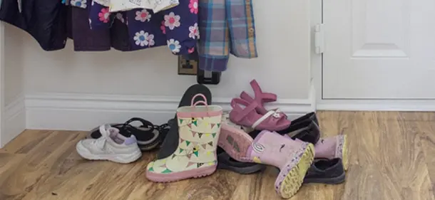A front entry way of a house with shoes and boots laying by the door and coats hanging above