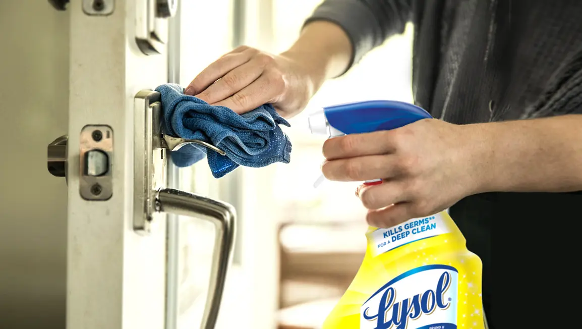 A bottle of Lysol Multi-Purpose cleaner and a cloth being used to clean a door latch.