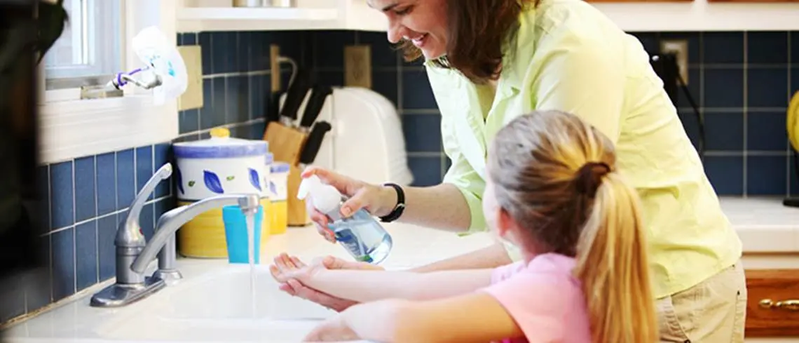 Adult applying soap to childs hand over kitchen sink
