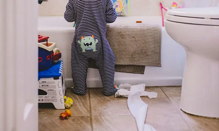 Baby standing in front of bathtub in messy bathroom