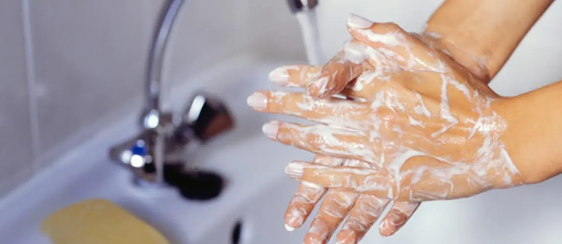 Adult hands covered in soap lather under bathroom faucet