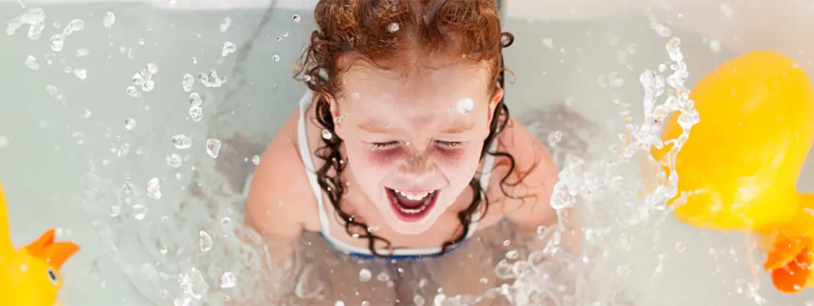 Child laughing in bath surrounded by rubber ducks