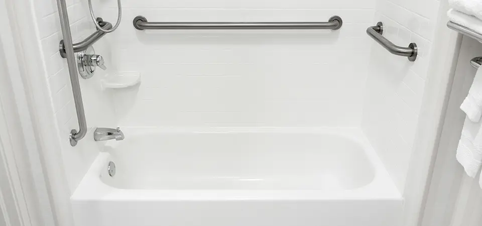 White bathroom containing a bath with shower and grab bars