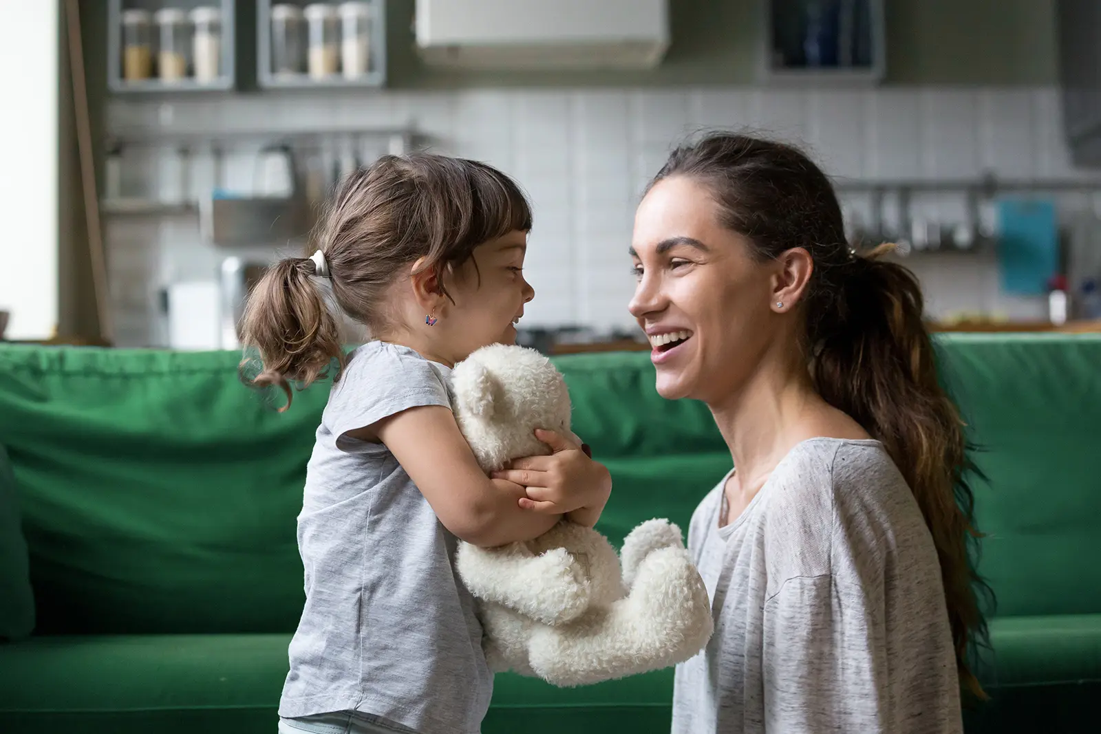 Child hugging stuffed bear smiles at kneeling parent