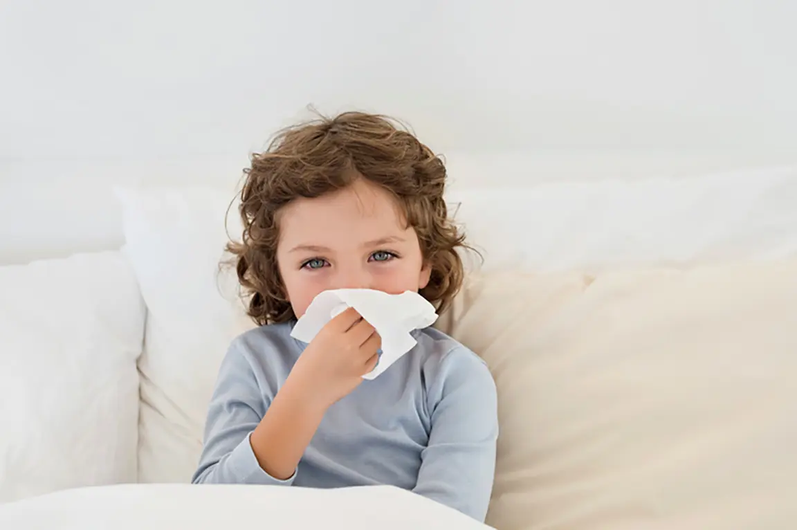 Sick child under blanket holds tissue to their face