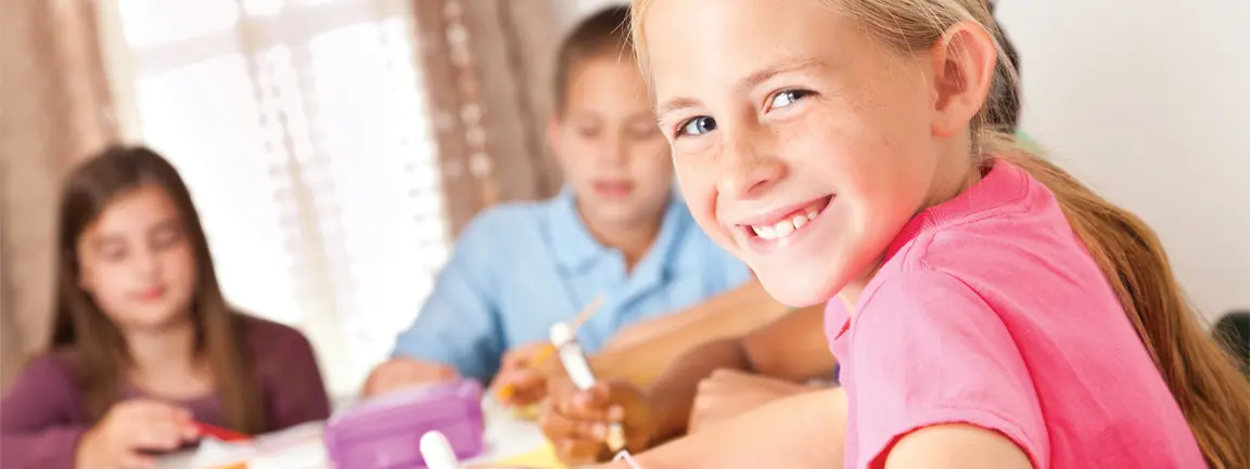 Child at desk with craft paper smiling at camera