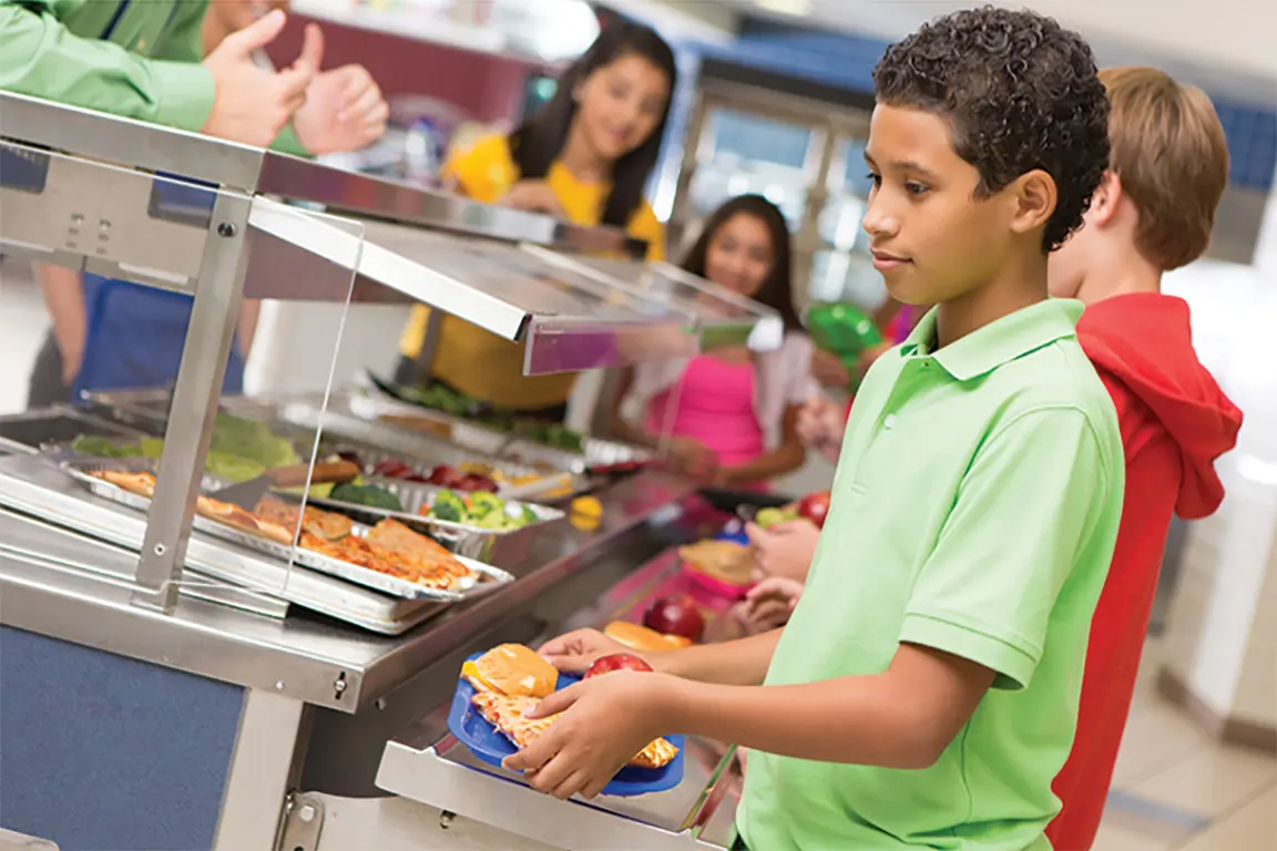 Child in school cafeteria holding lunch tray