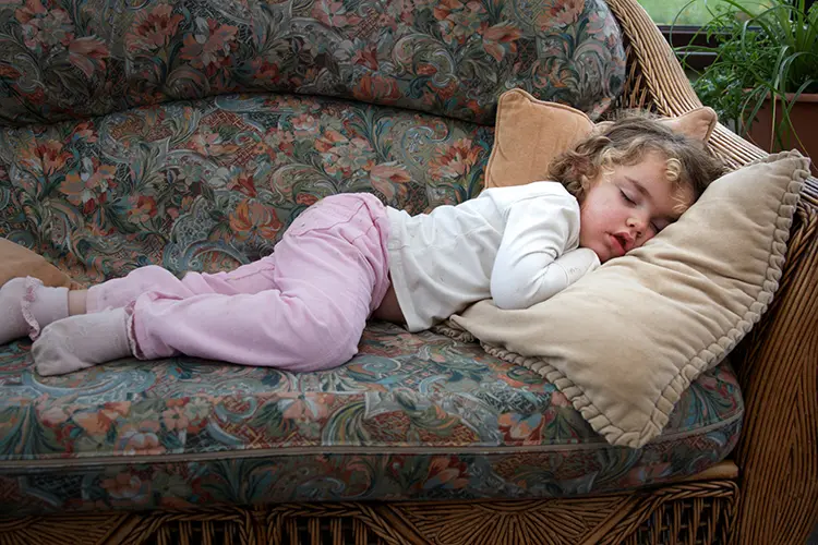 Child sleeping on sofa with head on a cushion