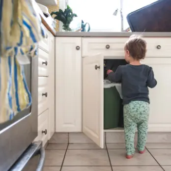 Young child approaches a trash can in a kitchen cupboard