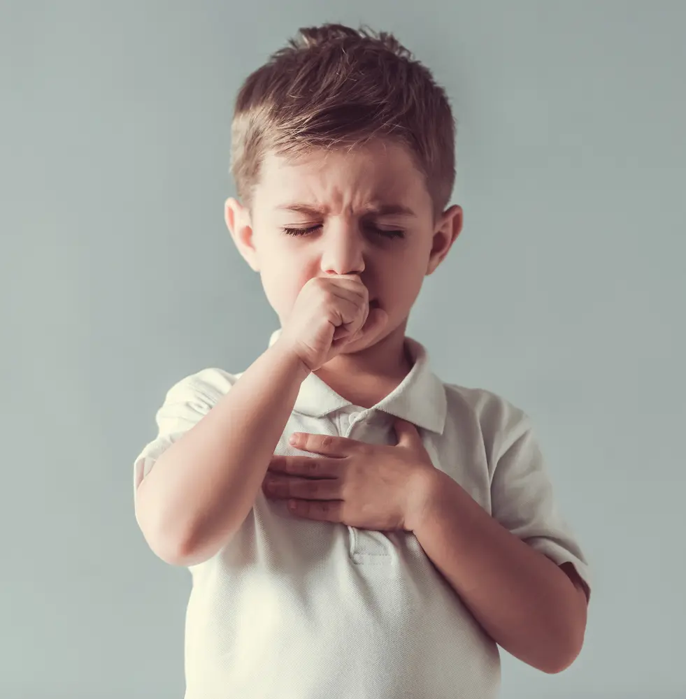 Frowning child holding one hand to chest and other to face while coughing