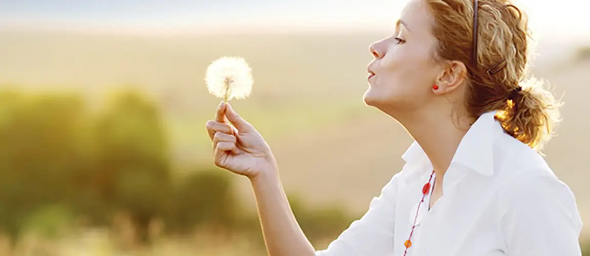 Adult standing in field blowing on white dandelion head