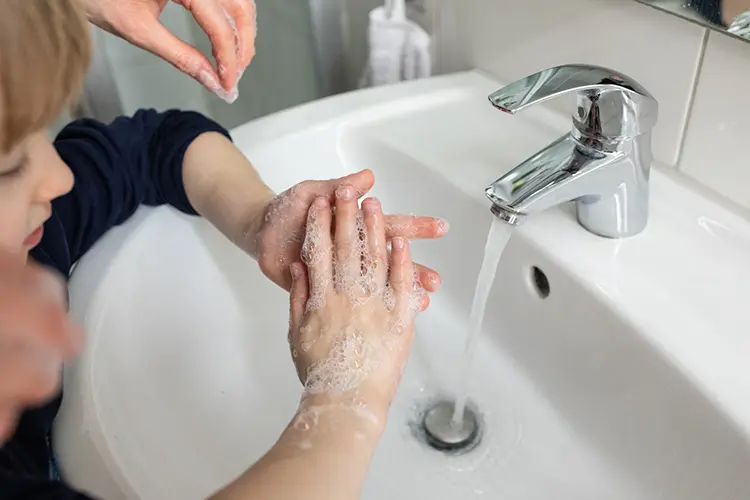Parent supervising child washing their hands in a bathroom sink