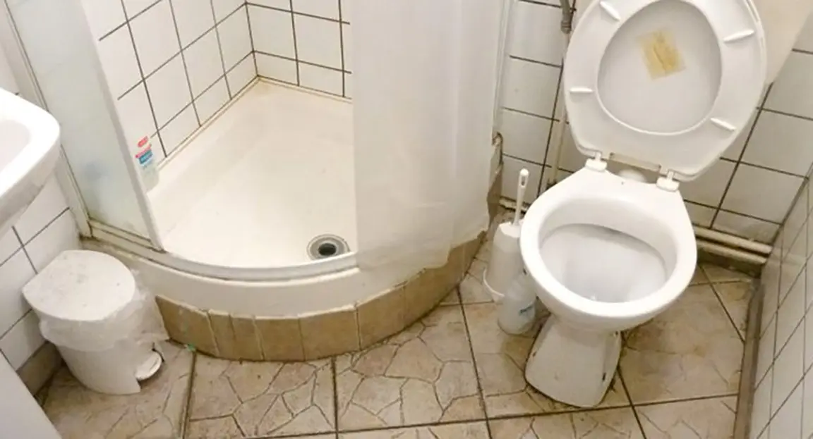 Dirty bathroom with porcelain tiles toilet and shower cubicle