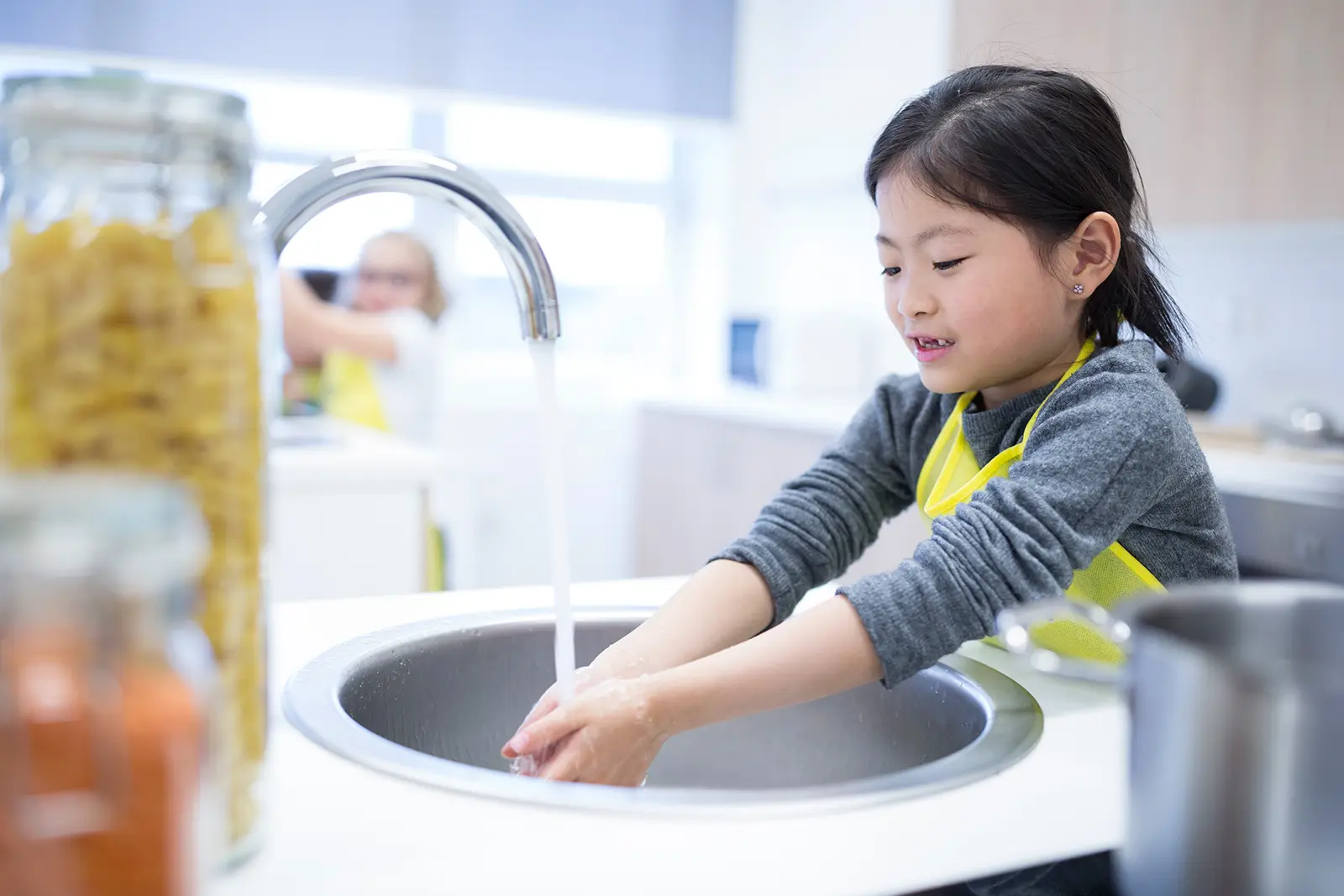 Child in apron washes hands at classroom sink