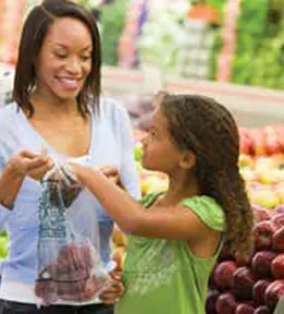 Parent and child holding fruit smile at each other in grocery store
