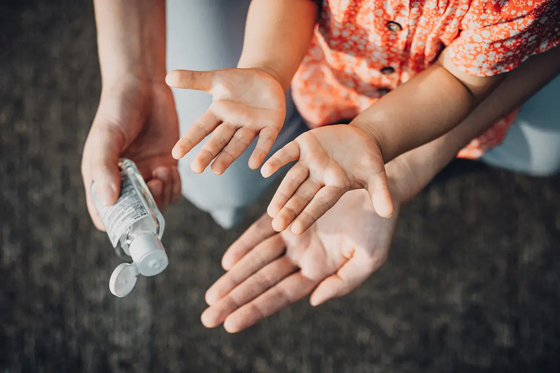 Mother squeezing hand sanitizer onto little daughter's hand outdoors to prevent the spread of viruses during the Covid-19 health crisis
