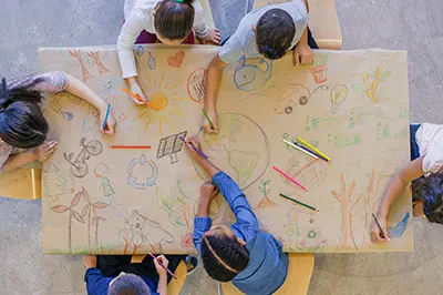 An aerial view of a multi ethnic group of children learn about going green and color in environmentally friendly concepts surrounding a drawing of Earth.
