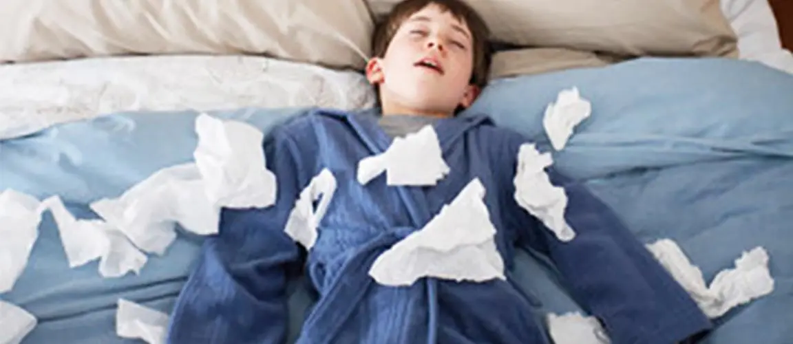 Sick child in robe lying on top of bed covered in used tissues