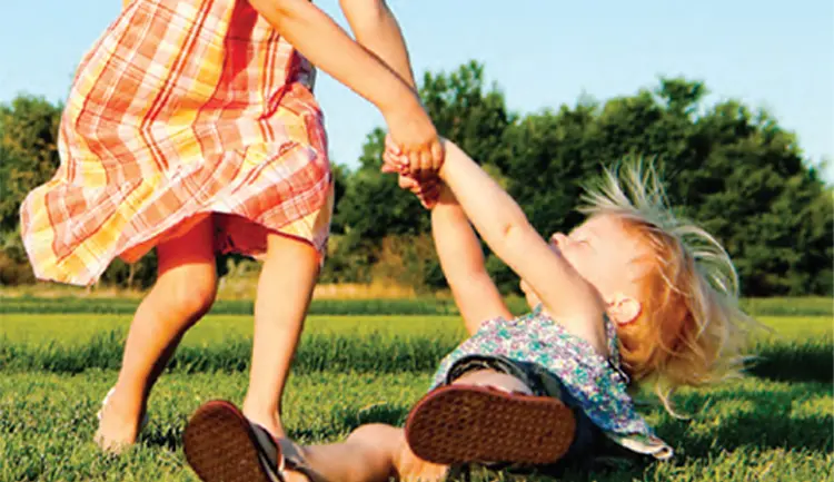 Children holding hands spinning in a circle in a field of grass