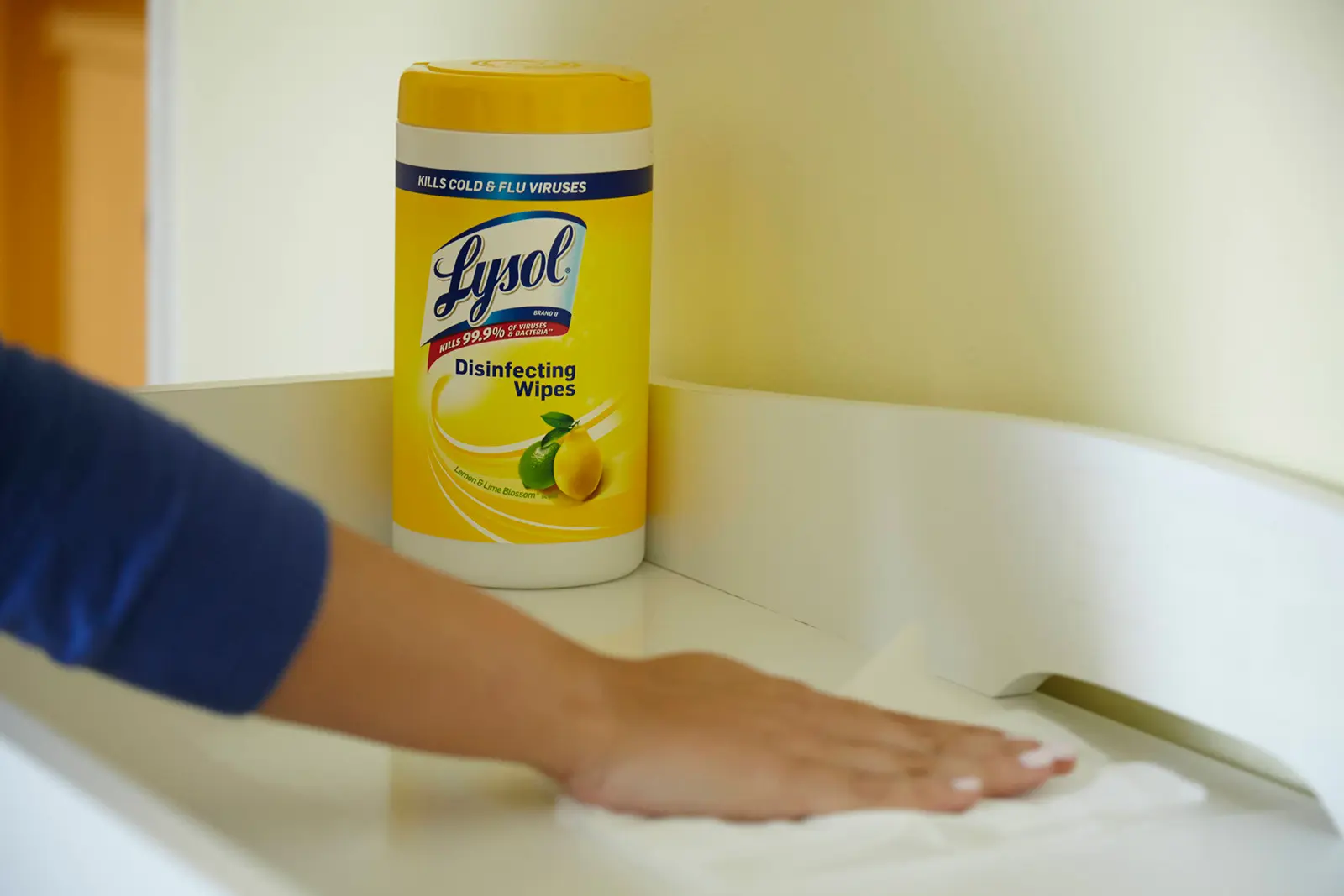 Arm wiping down white surface next to canister of Lysol Disinfecting Wipes