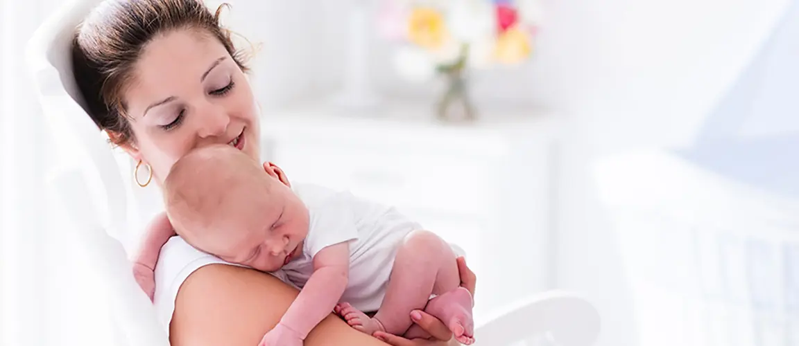 Parent looking tenderly towards young baby held sleeping in their arms