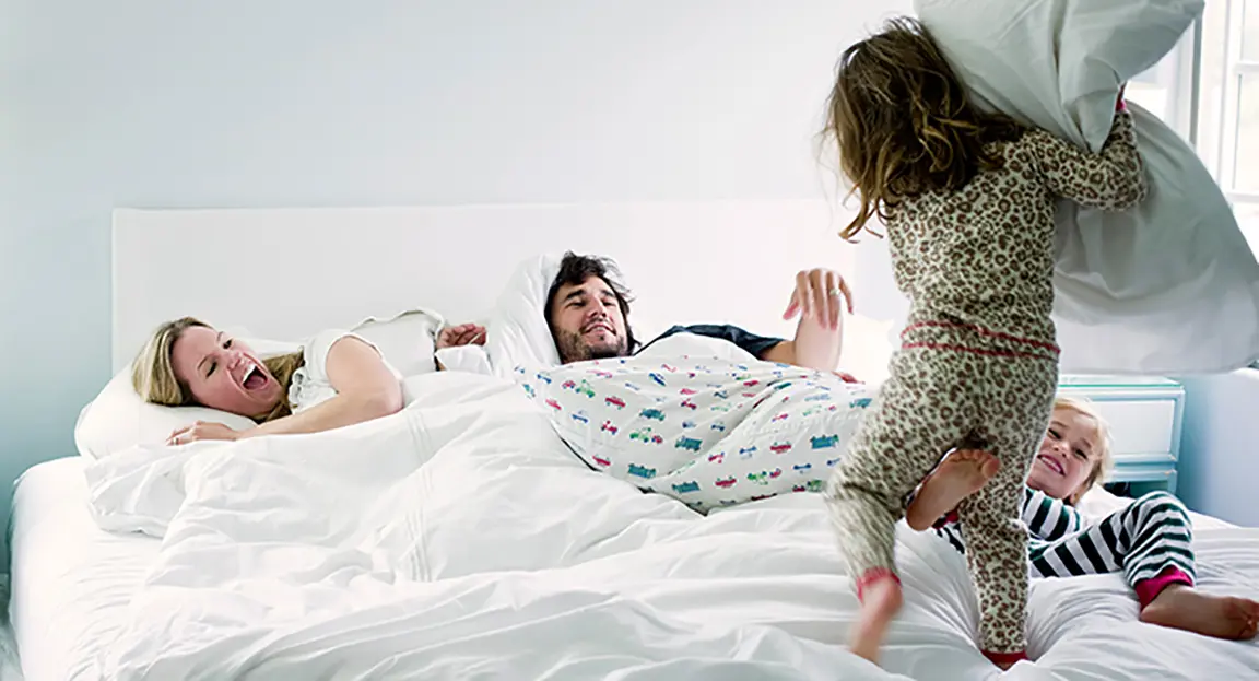 Children jumping on bed and threatening parents who are in bed with a pillow