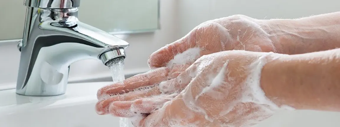 Adult with soap lathered hands holding them under running bathroom faucet