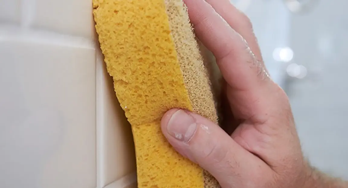 Person using sponge to wipe bathroom tiles