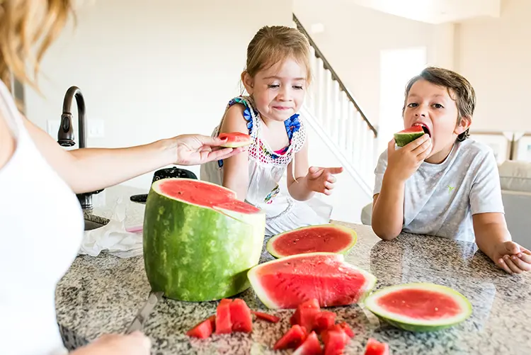 Parent and children eat watermelon on a kitchen counter