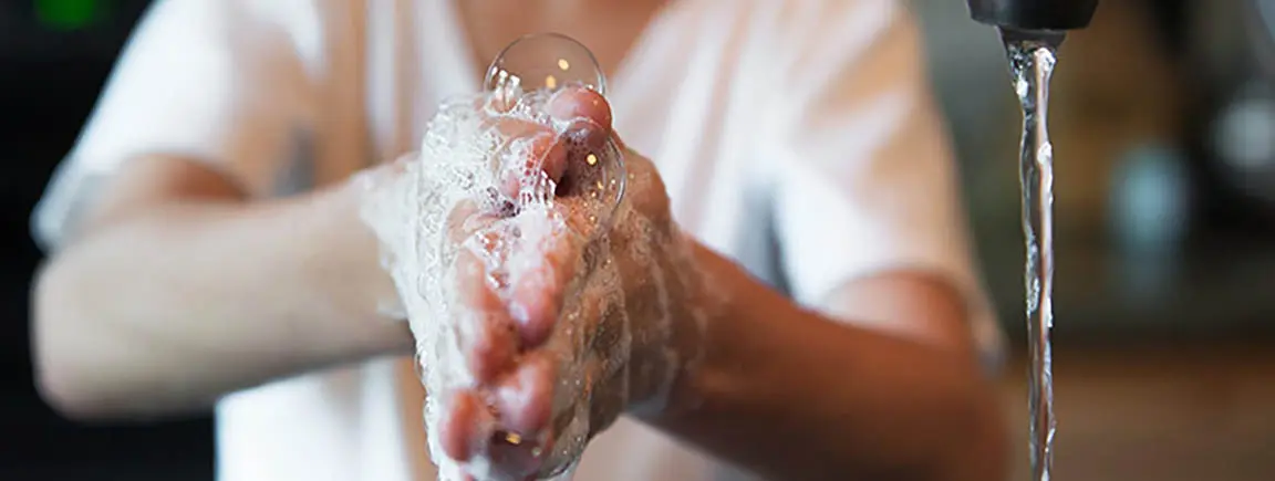 Torso of child lathering hands with soap next to running faucet