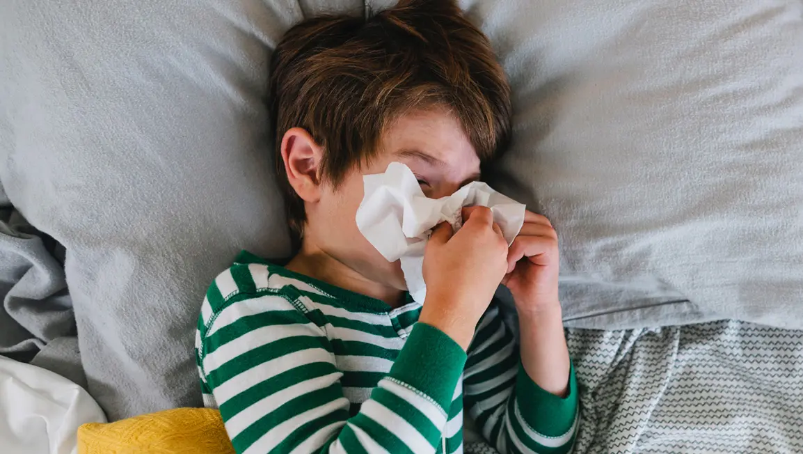 A child sick in bed holding a tissue to their nose