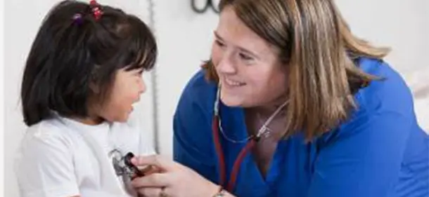 Nurse smiling and holding a stethoscope to the chest of small child