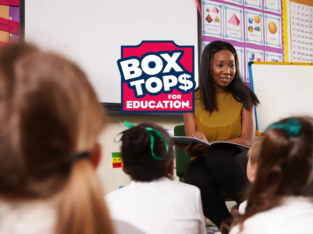 Funding for your school A teacher at the front of a classroom reading a book to a group of elementary students. Box Tops for Education Logo overlays the image.