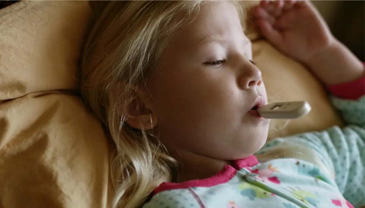 Child laying in a bed with a thermometer in their mouth